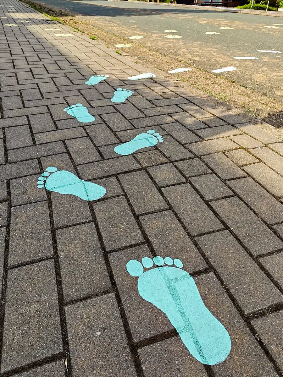 Turquoise voetstappen over het voetpad gaan als witte voetjes verder over de straat. Stap voor stap naar de overkant.