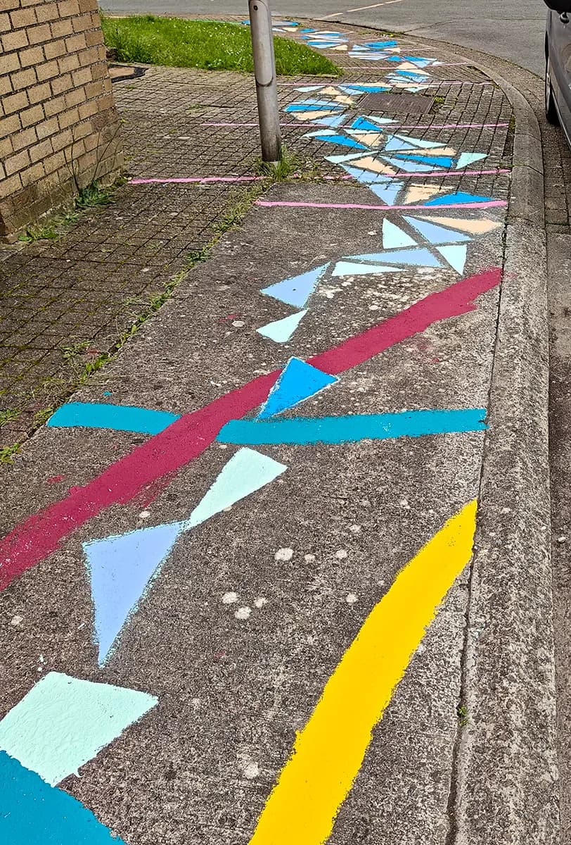 Blauwe, mintgroene en zalmkleurige driehoeken tussen rode, turquoise en gele lijnen die het voetpad rond de hoek volgen.